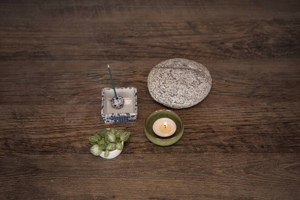 Wellness deco arrangement with burning candle, incense sticks, round stone and fresh leaves on wooden table, view from above. Mindfulness, meditation concept. Zen style background. - Fotoğraf, Görsel