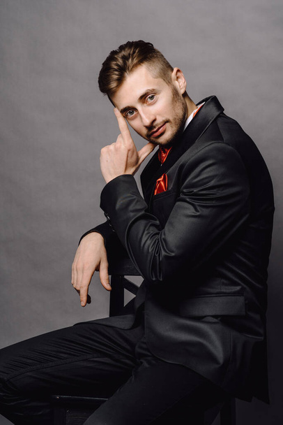 serious business man in elegant double breasted suit sitting on a chair on grey studio background - Фото, зображення