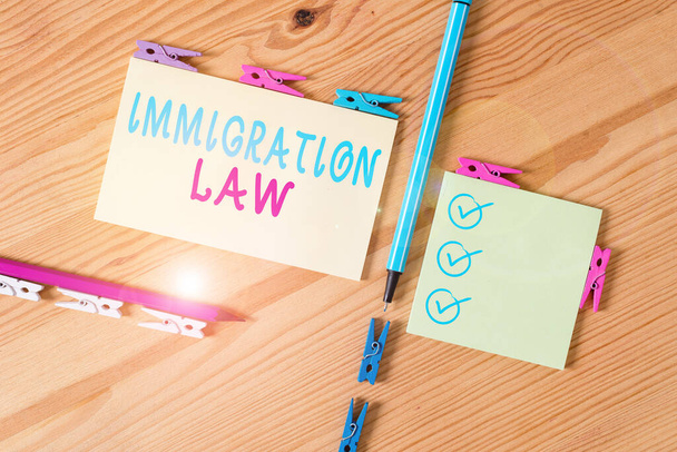 Szöveges jel, ami a bevándorlási törvényt mutatja. Üzleti fotó bemutató nemzeti jogszabályok és jogi precedensek a bevándorlás Színes ruhacsap papírok üres emlékeztető fa padló háttér iroda - Fotó, kép