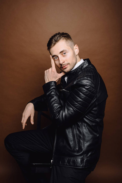 Handsome young man isolated. Fashionable man in leather jacket is standing on brown background. - Photo, Image