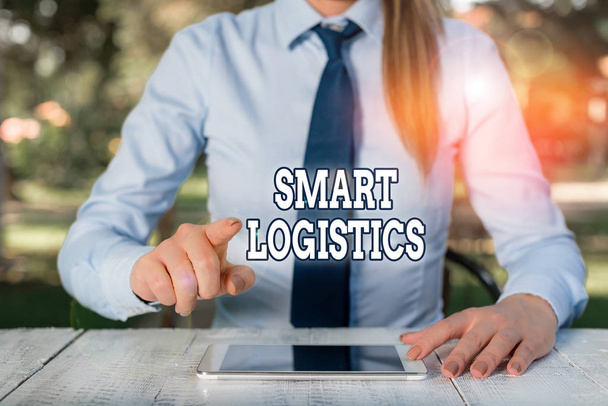 Εννοιολογική γραφή χεριών που δείχνει Smart Logistics. Business photo text integration of intelligent technology in logistics system Γυναίκα επιχειρηματίας που κάθεται δίπλα στο τραπέζι και κρατάει κινητό τηλέφωνο. - Φωτογραφία, εικόνα