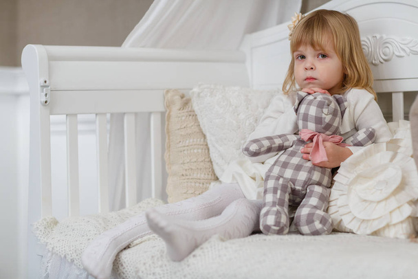 Sad pretty girl with toy bear sits on a sofa in the room. - Foto, Imagen
