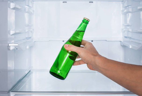 Male hand takes a bottle of beer in the fridge - Фото, изображение