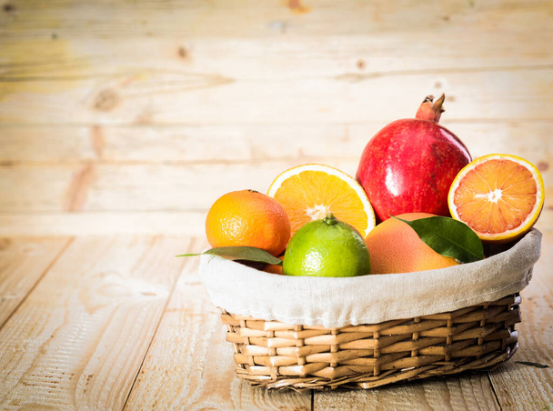 Small wicker basket of delicious assorted fresh fruit with an apple and a variety of citrus including a juicy halved orange on a wooden background - Foto, afbeelding