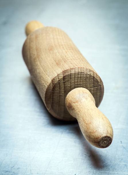 Closeup view to the handle of an old-fashioned wooden rolling pin standing at an oblique angle on a blue toned background with vignetting - Фото, изображение
