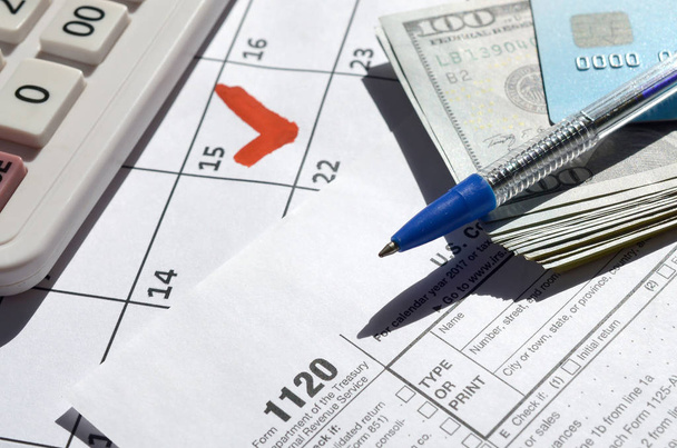 1120 Vennootschap Inkomstenbelasting blanco met dollarbiljetten, rekenmachine en pen op kalenderpagina met gemarkeerde 15 april - Foto, afbeelding