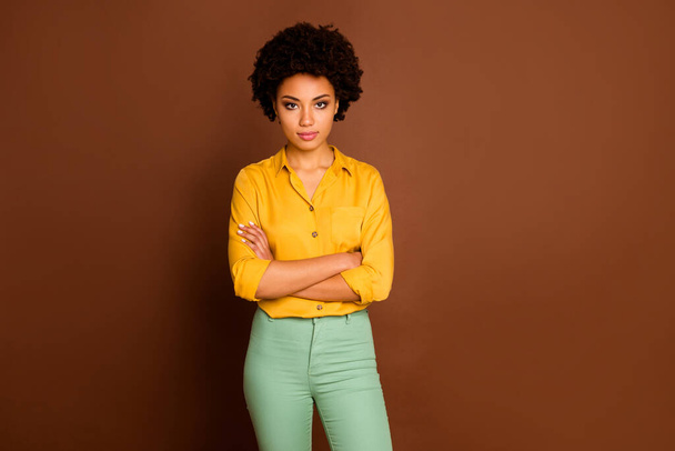 Photo of beautiful business dark skin curly lady looking strictly colleagues bad mood confident person arms crossed wear yellow shirt green pants isolated brown color background - Foto, afbeelding