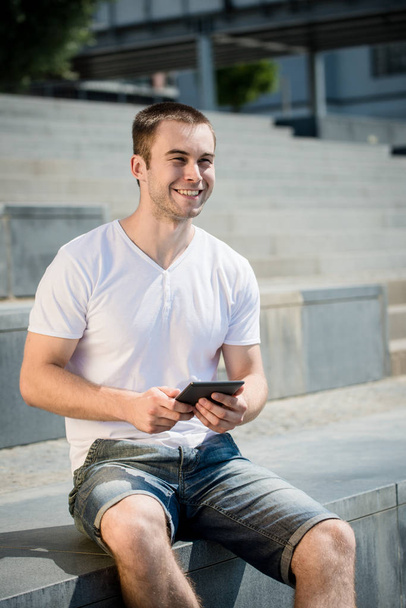 Young smiling man working with tablet - outdoor in town - Фото, изображение