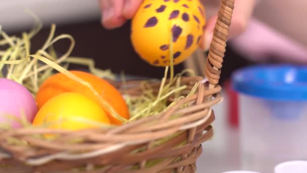 Happy easter. Little girl painting Easter eggs. Close-up of a girls hand putting a painted egg in a basket. Cute little child girl wearing bunny ears on Easter day. - Séquence, vidéo