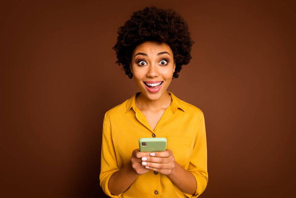 Portrait of astonished afro american girl use smartphone read wonderful social media news impressed scream wow omg wear yellow good look clothes isolated over brown color background - Фото, зображення