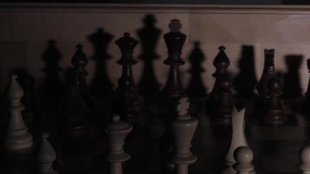 Schaduwen van schaken in het donker. Schaakbord met stukken. Schaduw van schaakstukken op een donkere achtergrond. Schaduwen van schaken op een schaakbord. Licht verlicht schaakstukken. - Video