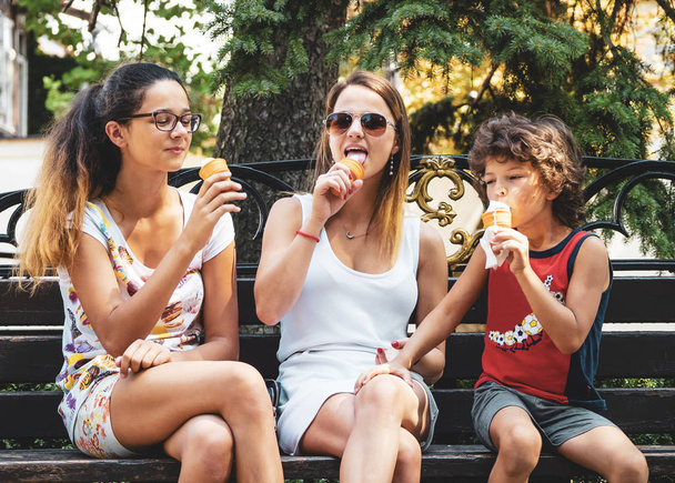 Group of four happy children eating ice cream together outdoor.three adorable children eating ice cream sitting on a wooden bench in the park. fun holiday concept - Foto, afbeelding