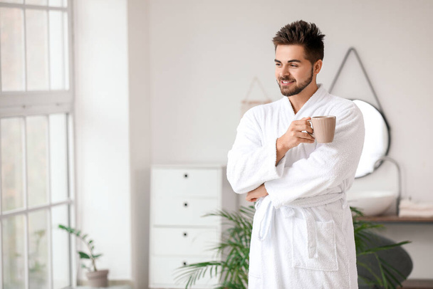 Handsome young man drinking tea in bathroom - Photo, Image