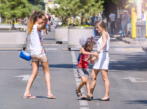 A boy walks with his older sisters on the street on a warm summer day. Expression of love and support for sisters to little. Love between mother, daughter and son. - Zdjęcie, obraz