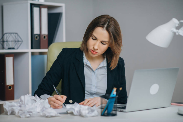 Businesswoman typing his piece of art, crumpling and wasting a sheet of paper dissatisfied with result. Crumpled pieces of paper - Foto, imagen