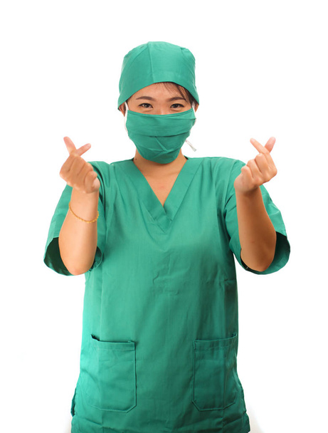young beautiful and happy Asian woman medicine doctor or chief hospital nurse in green scrubs and surgeon hat smiling confident doing love finger sign - Photo, Image