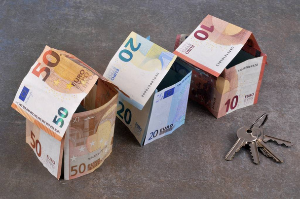 Haus in Euro-Banknoten mit einem Schlüsselbund vor grauem Hintergrund - Foto, Bild