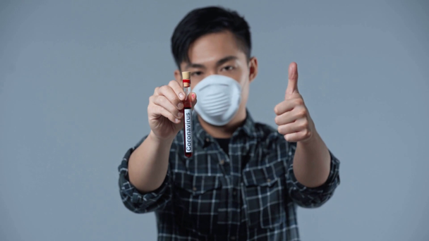 rack fókusz ázsiai férfi gazdaság minta koronavírus betűkkel és mutatja hüvelykujj fel izolált szürke  - Felvétel, videó