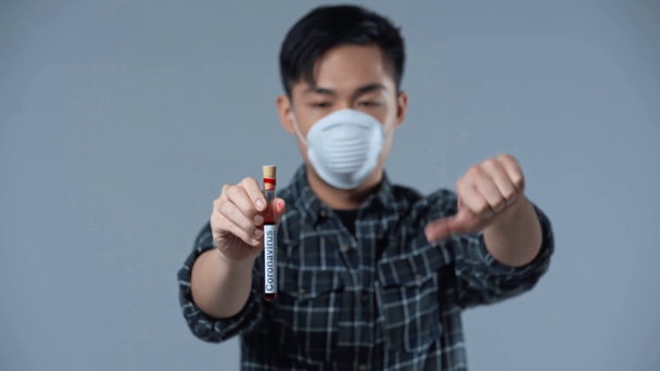 racku zaměření asijské muž drží vzorek s koronasvirus nápisy a ukazující palec dolů izolované na šedé  - Záběry, video