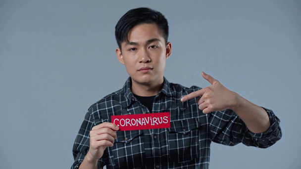 asiático hombre apuntando con dedo a coronasvirus lettering aislado en gris
  - Metraje, vídeo