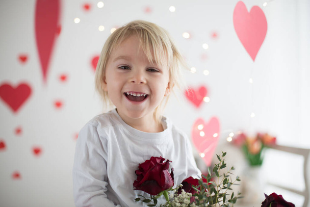 Cute blonde toddler boy, holding box in heart shape and flowers - Foto, imagen