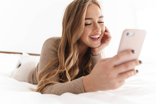 Photo of young happy woman smiling and using cellphone while lying - Fotoğraf, Görsel