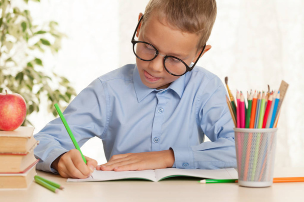 Молодой школьник сидит за столом и делает домашнее задание. Концепция начального образования - Фото, изображение