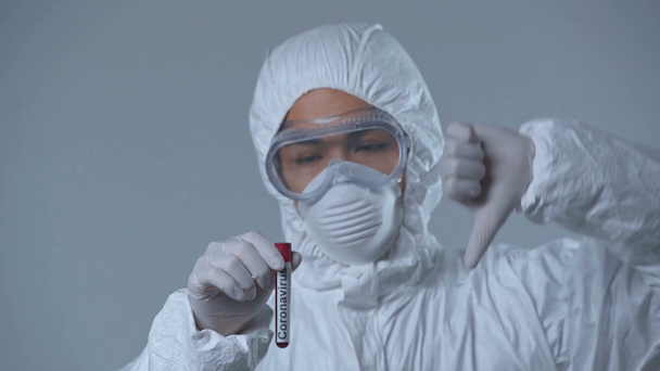 Ασιάτης επιστήμονας που δείχνει τον αντίχειρα προς τα κάτω και κρατώντας σωλήνα δοκιμής απομονωμένο σε γκρι  - Πλάνα, βίντεο