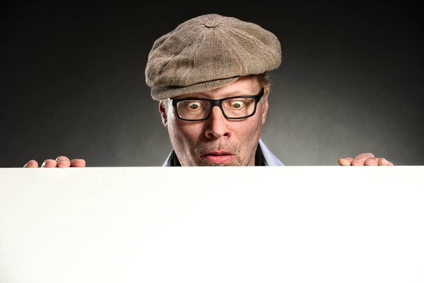 retrato de un hombre gracioso con gafas sosteniendo un cartel blanco sobre un fondo negro - Foto, Imagen