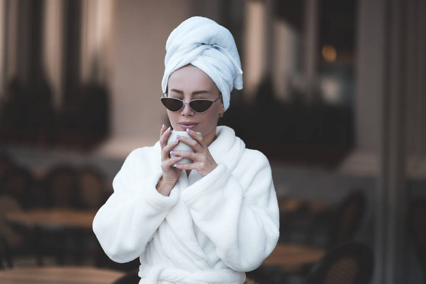 Stylish woman wearing cozy bathrobe drinking hot coffee in cafe closeup. Good morning.  - Фото, зображення