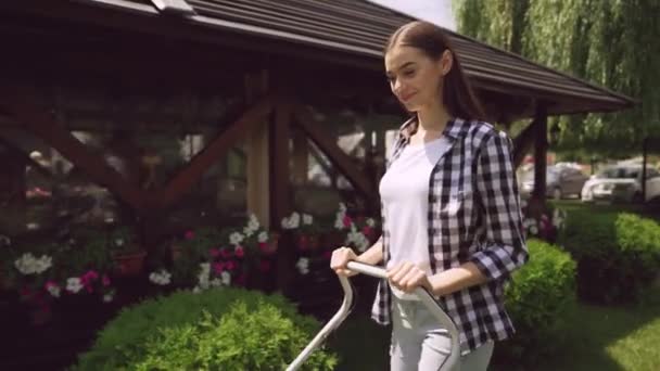 Beautiful girl cutting grass with lawnmower during sunny day - Кадри, відео