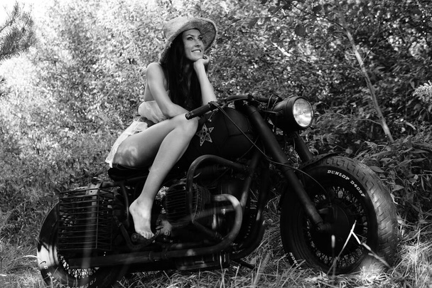 young sexy woman with long wavy hair in leather clothes and sunglasses posing near a motorcycle. Black and white photo. - Foto, Imagen