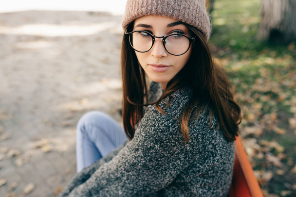 Close-up portrait of smart young woman smiling broadly, wearing transparent eyeglasses, gray sweater and pink hat. Outdoor image of pretty student girl relaxing in the city street. - Fotoğraf, Görsel