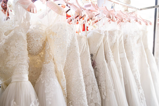 Krásné, bílé svatební šaty textury na pozadí. Svatební šaty visící na věšáku uvnitř svatebního salonu. Design, módní moderní luxus v detailu. - Fotografie, Obrázek