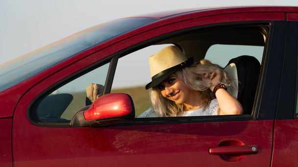 Mooie sexy blonde vrouw, rode auto, veld - Foto, afbeelding