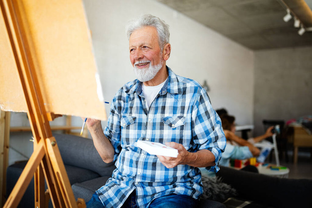 Handsome senior man artist paints on canvas painting on the easel - Foto, imagen