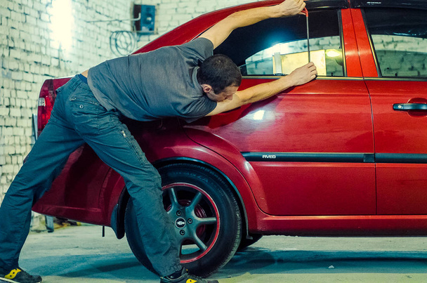 ένας μηχανικός με κουκούλα επισκευάζει ένα όχημα στο αυτοκίνητο - Φωτογραφία, εικόνα