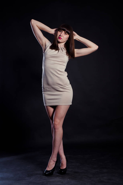 όμορφη μελαχρινή κοπέλα σε κοντό μπεζ φόρεμα ποζάρουν στο στούντιο  - Φωτογραφία, εικόνα