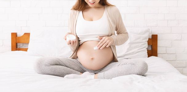 Pregnant woman moisturizing her belly with lotion, panorama - Valokuva, kuva