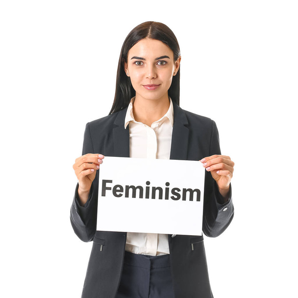 Joven empresaria sosteniendo papel con texto FEMINISMO sobre fondo blanco
 - Foto, Imagen