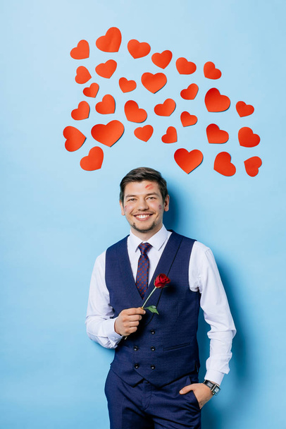 handsome caucasian guy with red rose isolated over blue background - Foto, immagini