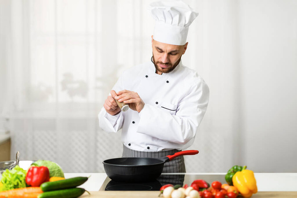 Chef toevoegen van peper in pan kruiden schotel in de keuken - Foto, afbeelding