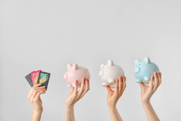 Female hands with credit cards and piggy banks on light background. Concept of online banking - 写真・画像