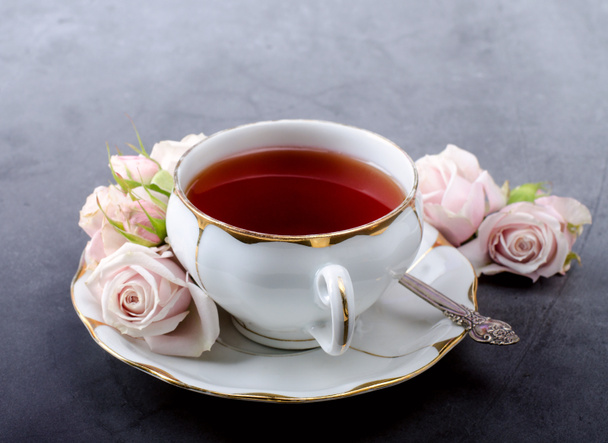 Tea time backdrop with vintage white porcelain tea cup, gentle pink roses on a dark gray background. - Photo, Image