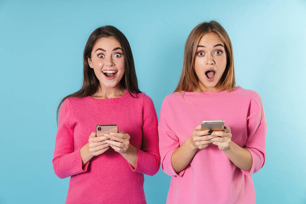 Photo of surprised nice women typing on cellphones and smiling - Zdjęcie, obraz