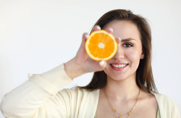 Νεαρό κορίτσι που κρατά ώριμο πορτοκάλι απομονωμένο σε ανοιχτό φόντο - Φωτογραφία, εικόνα