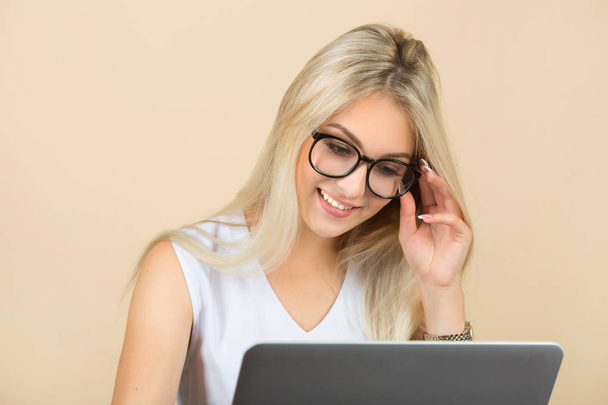 beautiful young woman in glasses on a beige background with a laptop - Zdjęcie, obraz