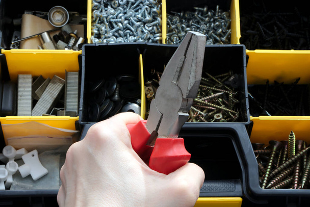 Набір інструментів у пластиковій коробці, плоскогубці в руці
. - Фото, зображення
