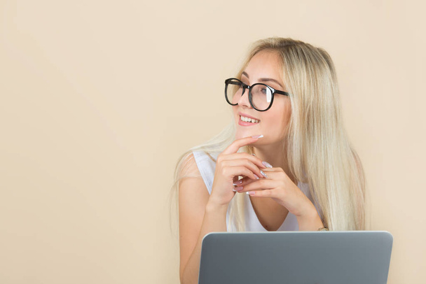 beautiful young woman in glasses on a beige background with a laptop - Фото, изображение
