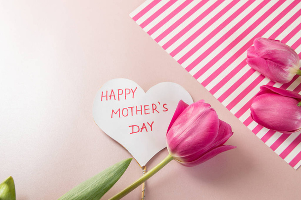 Delicate pink background with flowers of tulips, a card, a heart that says mother's day. Women's day. Postcard for Valentine's Day, on March 8 - 写真・画像
